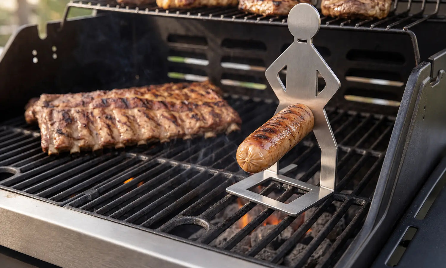 MeatRider Bratwursthalter aus Edelstahl mit gegrillter Bratwurst auf dem Grill als praktisches BBQ-Zubehör für gleichmäßiges Grillen.